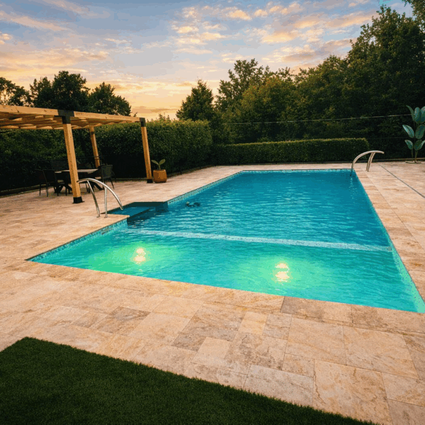 Rectangular swimming pool with turquoise water and underwater lights surrounded by a stone patio at sunset.